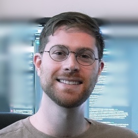 Shane Poole, smiling, in glasses and a tan sweater